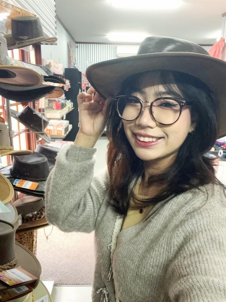 Thiri trying on a wide-brimmed felt hat in a hat shop
