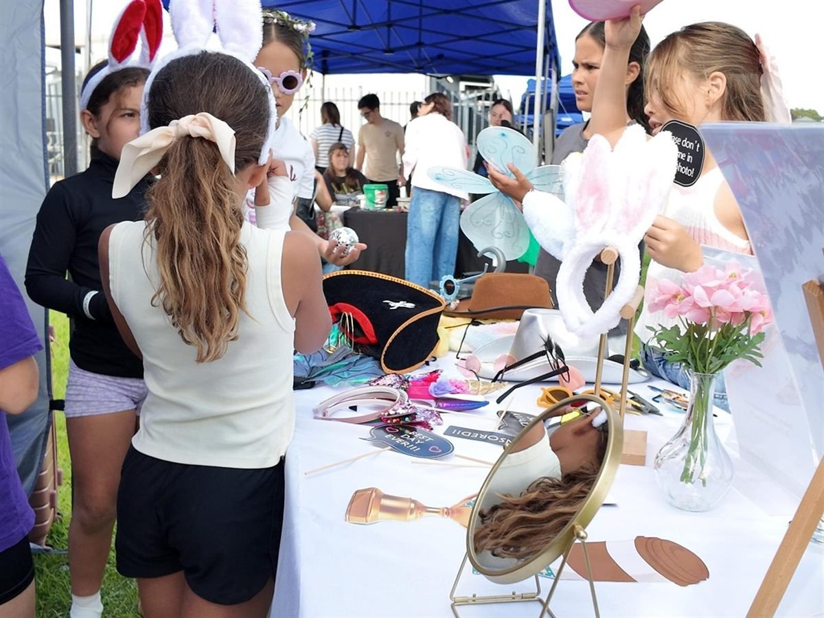 Children choosing from the Fotobooth Perth prop table at a community fundraising event, with bunny ears, hats, fairy wings, novelty glasses and speech-bubble signs laid out