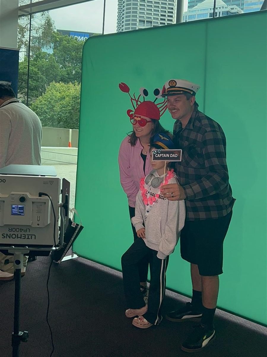 A family posing with novelty props in front of the Fotobooth Perth green screen at the Perth Boat Show, with studio lighting to one side