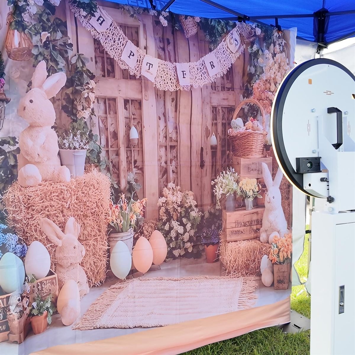 An open air Fotobooth Perth booth at an outdoor Perth event, the camera facing the room with no enclosure around it, beside a printed Easter-themed backdrop