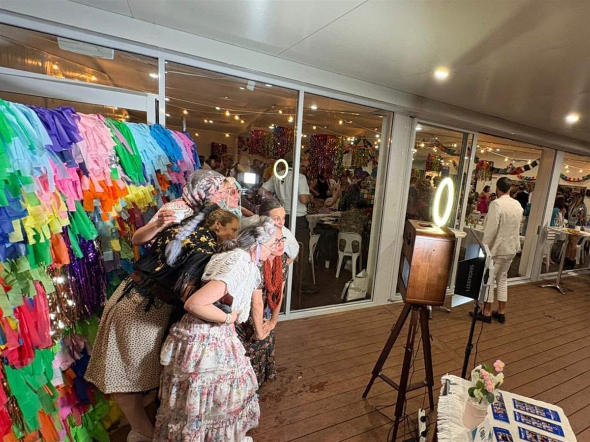 Guests posing at a Fotobooth Perth booth at a Perth event, with freshly printed photo strips laid out on the table beside it